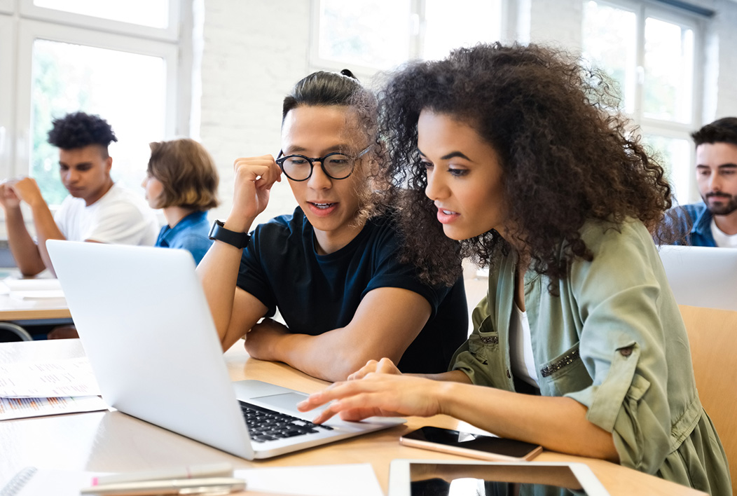 Male and female college students sitting at a table looking at a laptop.