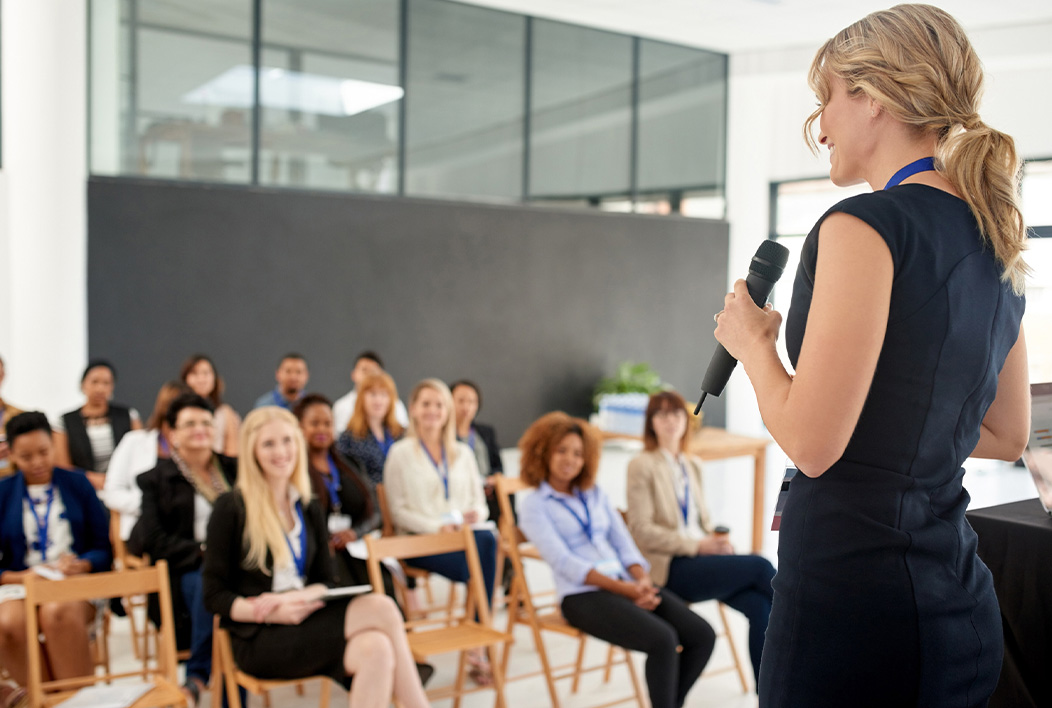 Female lecturer holding microphone talking to attendees.