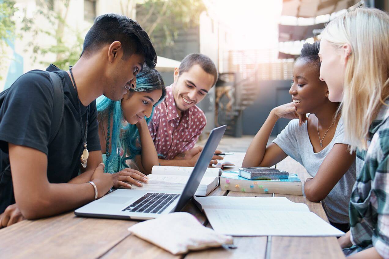 Five college students sitting outdoors at a picnic table studying.